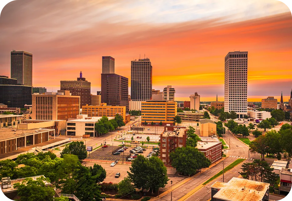City skyline at sunset with modern high-rise buildings and vibrant orange sky.