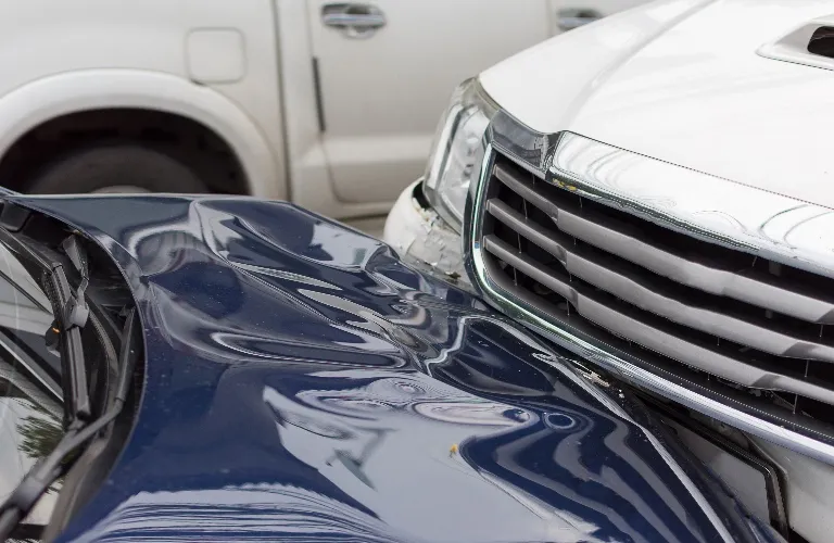 Close-up of a white and dark blue vehicle involved in a front-end collision.