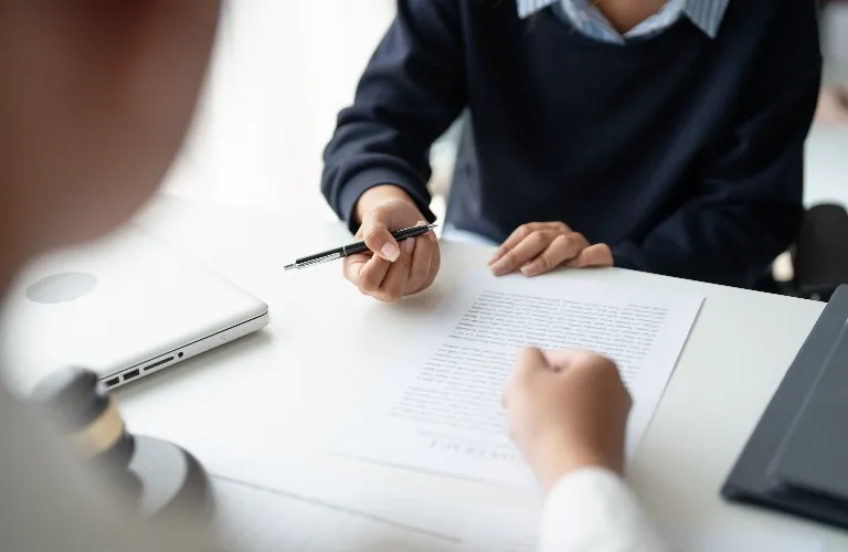 Two individuals reviewing a printed document at a white desk with a laptop and pen.