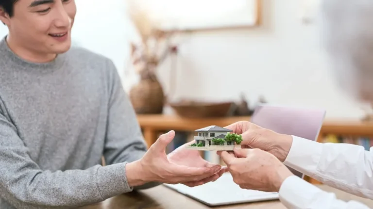 Two people exchanging a small detailed house model in a bright office setting.