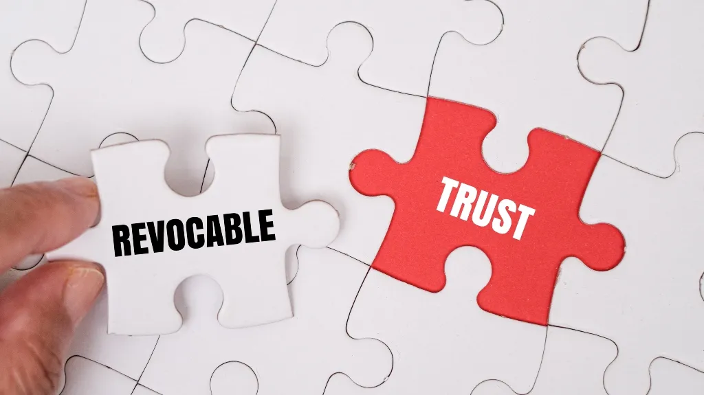 Hand holding a white puzzle piece labeled "REVOCABLE" near a red puzzle piece labeled "TRUST" on a white puzzle background.