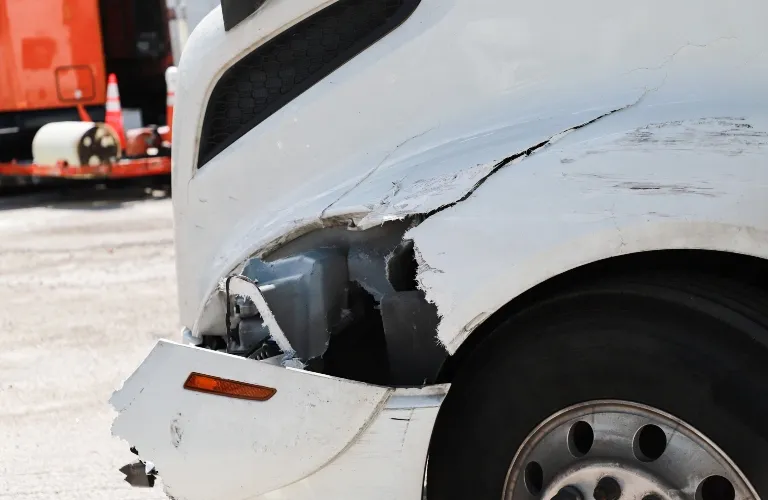 Close-up of a white vehicle's front right side with extensive damage and a detached bumper.