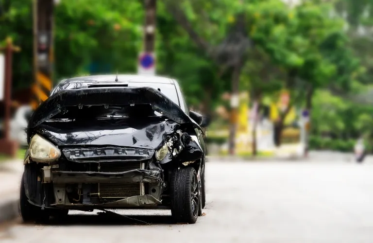 Front view of a black car with extensive collision damage on the hood and right headlight.